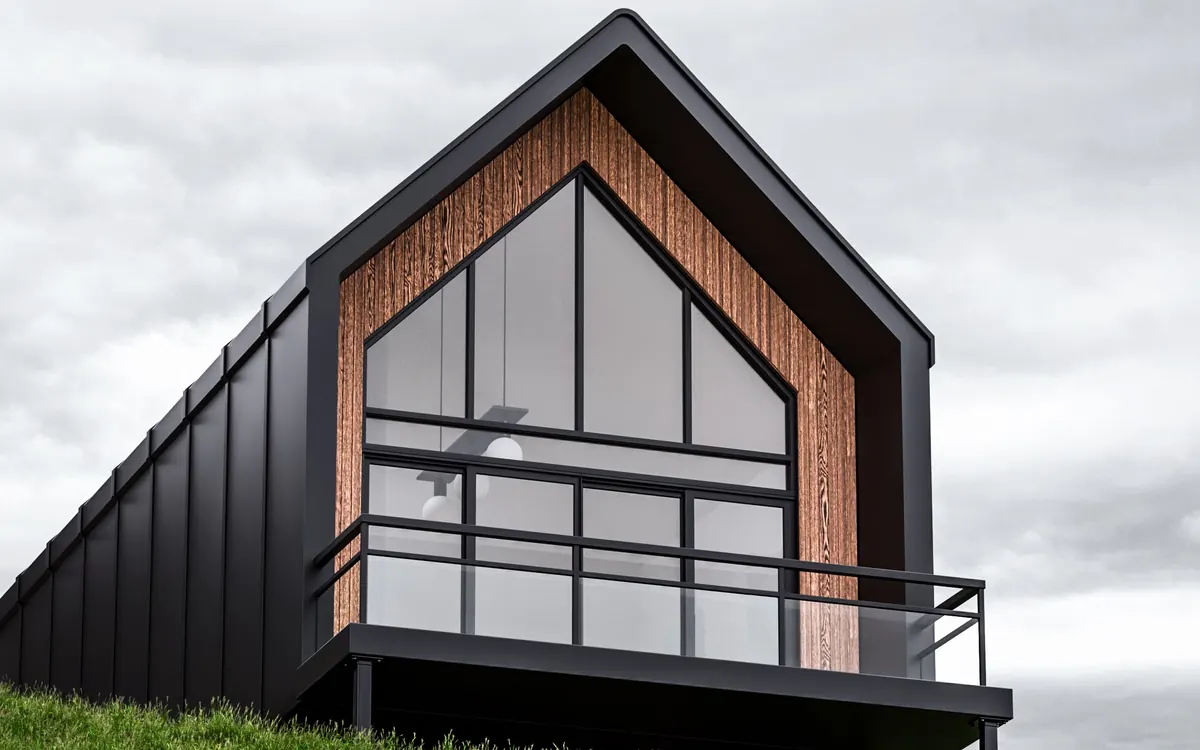 Contemporary house with a dark gable roof, timber-clad facade and glass balcony on a grassy hillside